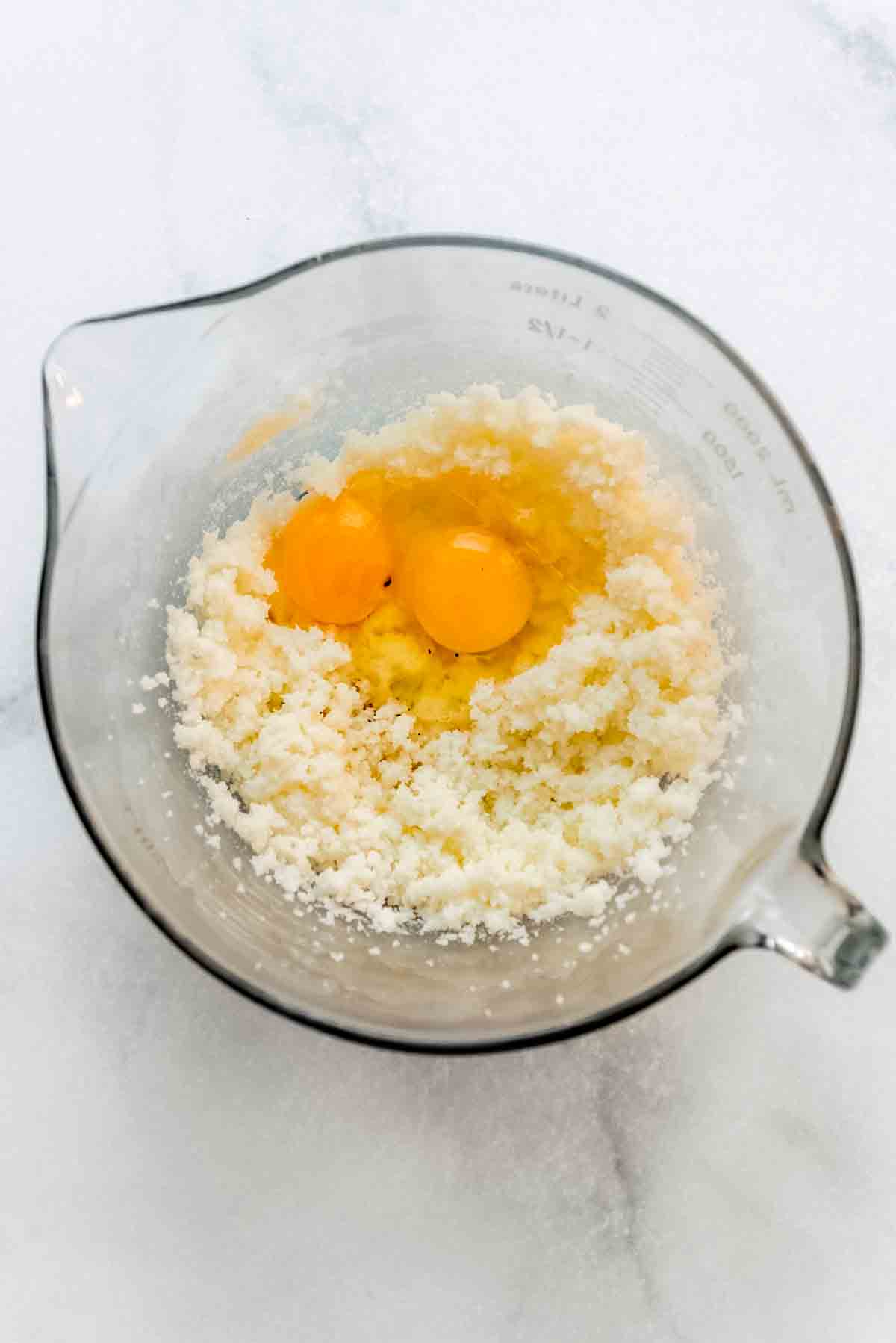 Eggs and vanilla have been added to the fluffy mixture in the glass bowl, waiting to be blended. 