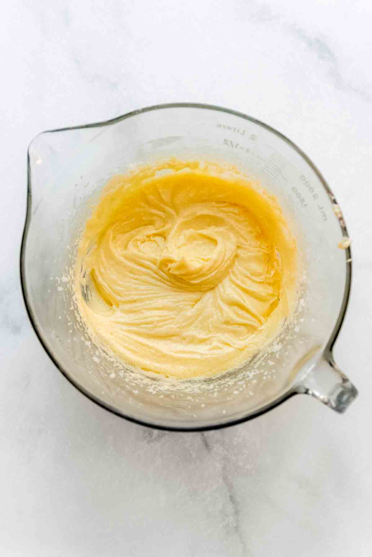 A blended, smooth mixture in a soft yellow shade is at the bottom of a glass mixing bowl. 