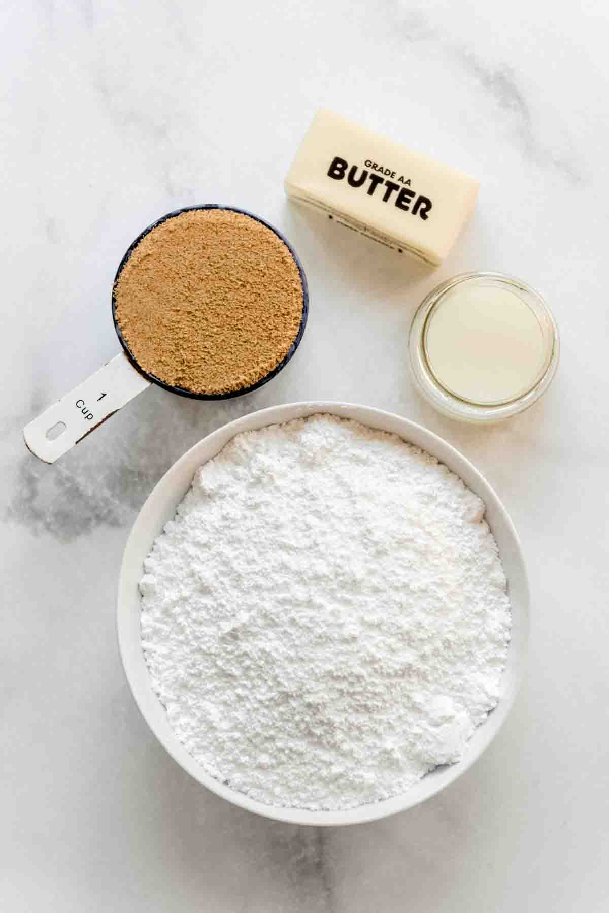 Ingredients for penuche frosting are displayed in individual bowls on a white marbled surface. 