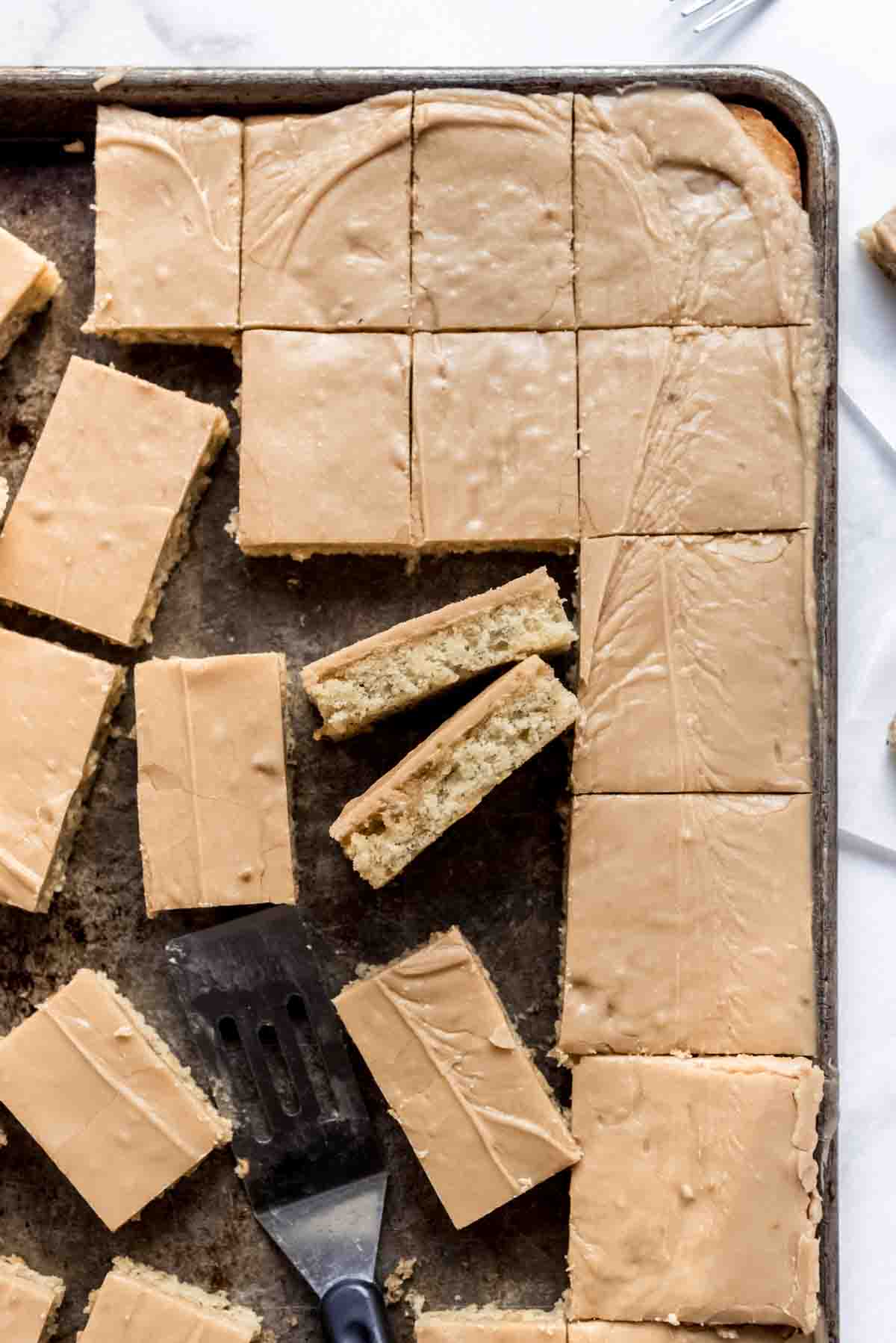 A baking sheet with slices of soft banana sheet cake covered in penuche frosting.