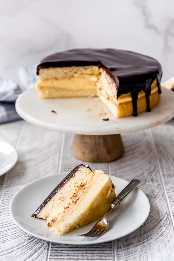 a slice of boston cream pie in front of the rest of the cake on a cake stand