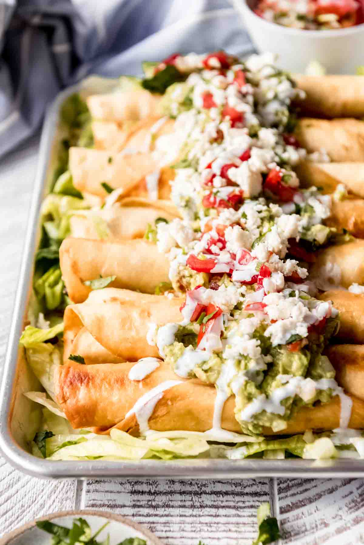 A close image of flautas topped with guacamole, pico de gallo, and other toppings.