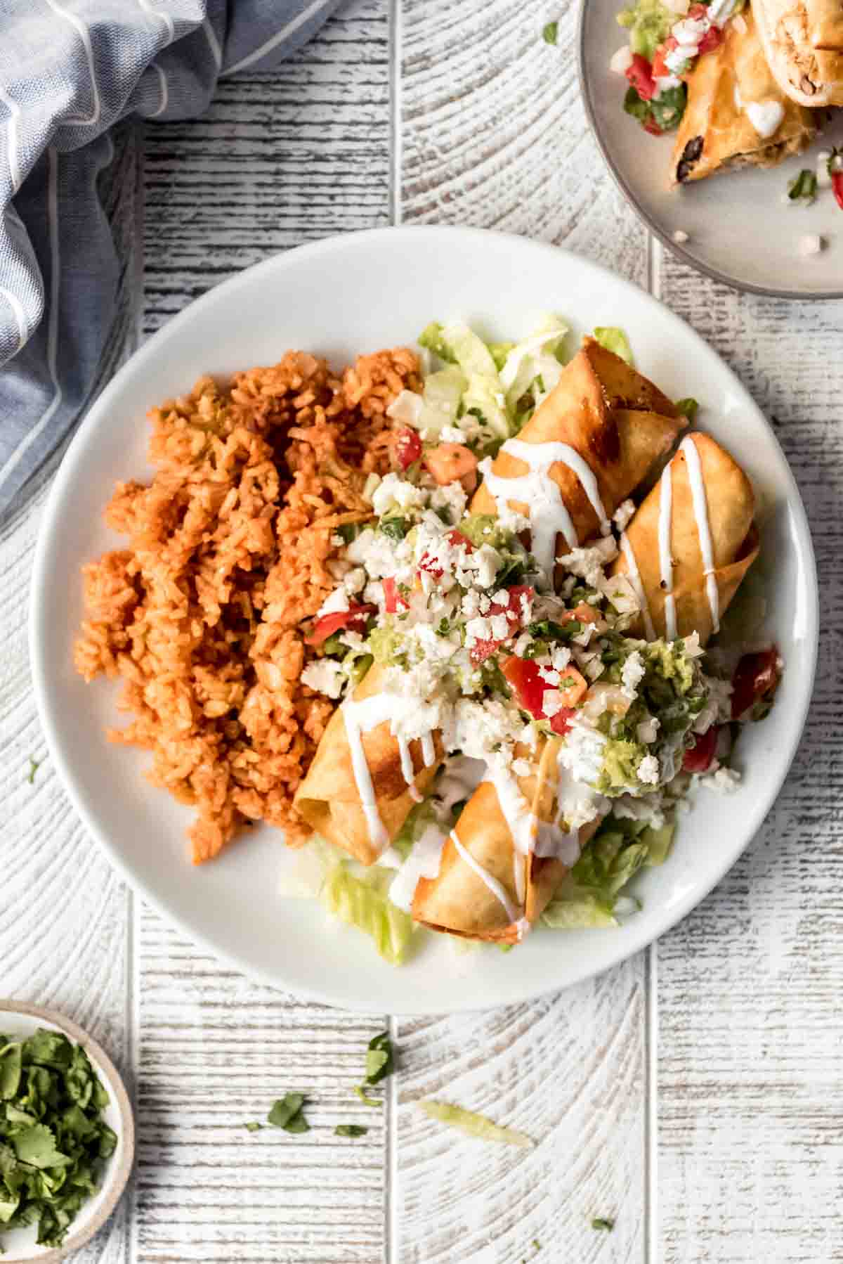 A white plate with Mexican rice and chicken flautas.