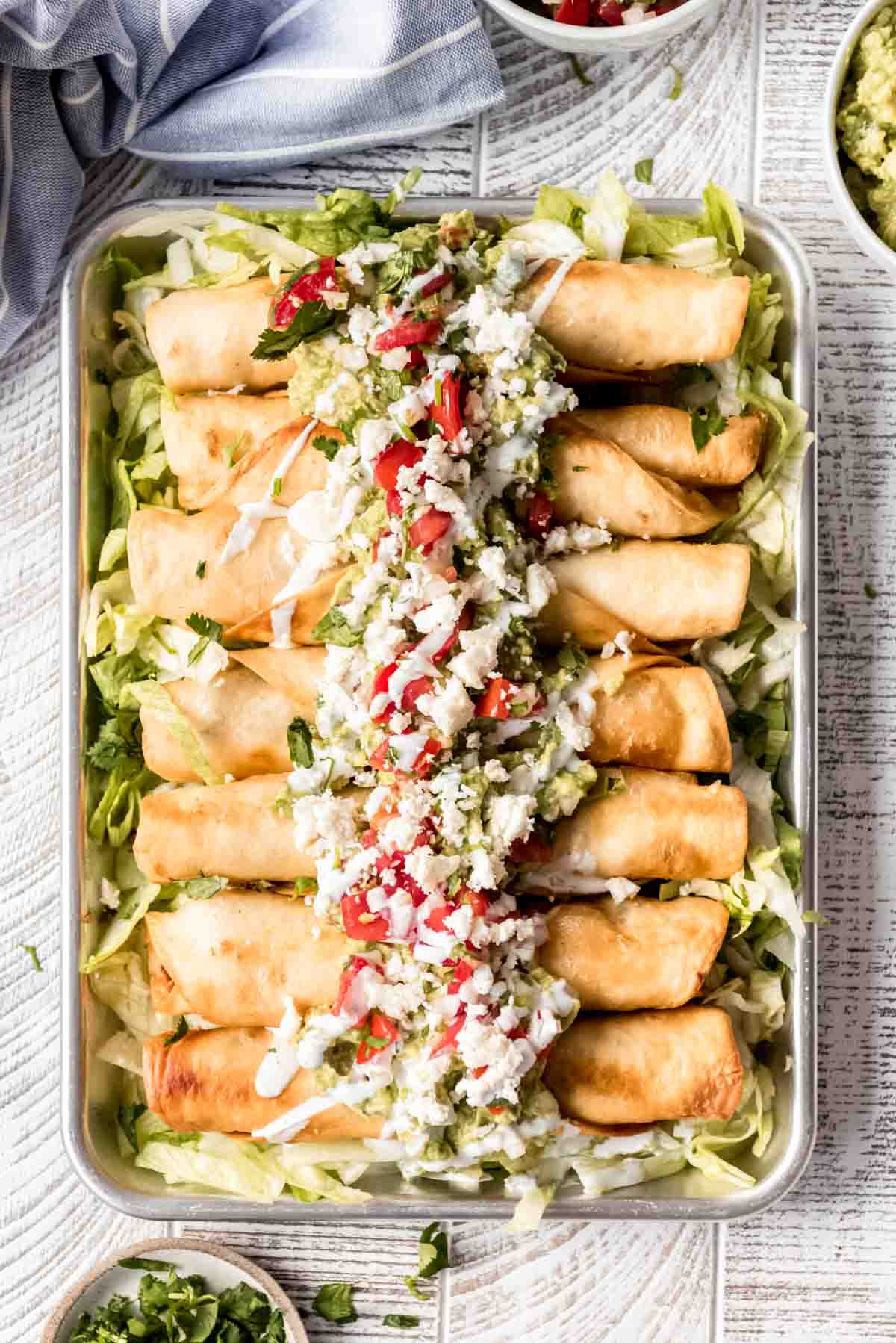 Chicken flautas arranged on a bed of lettuce with guacamole, pico de gallo, Mexican crema, and queso fresco on top.