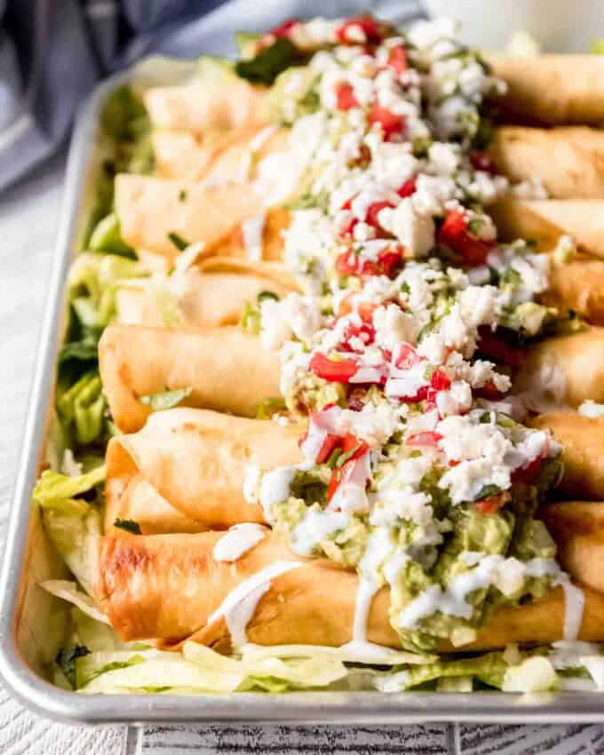 A close image of flautas topped with guacamole, pico de gallo, and other toppings.