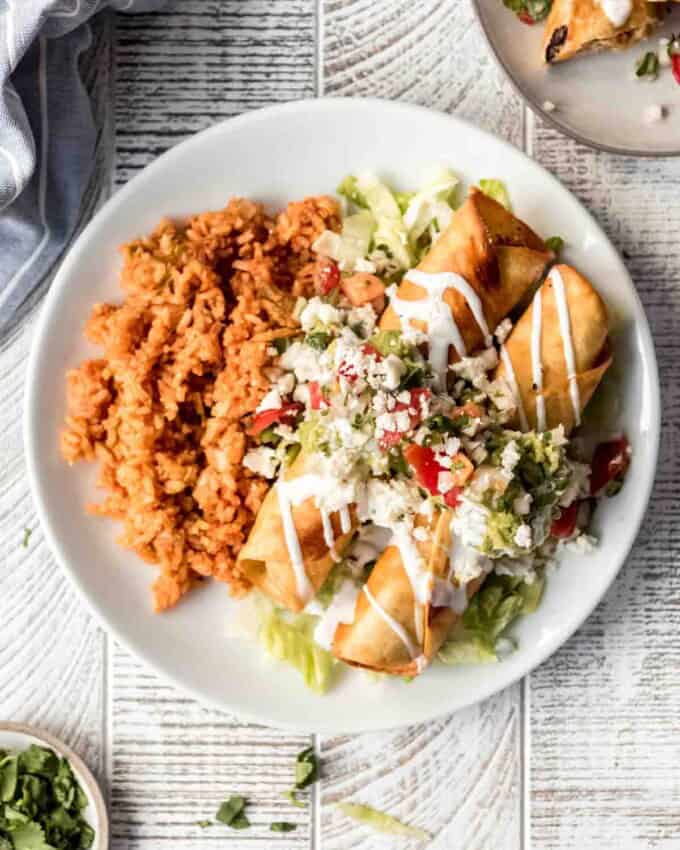 A white plate with Mexican rice and chicken flautas.