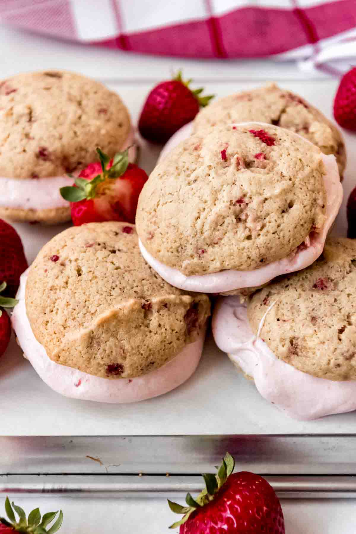 Prepared Strawberry Whoopie Pies are stacked on a tray, with whole strawberries scattered around them. 