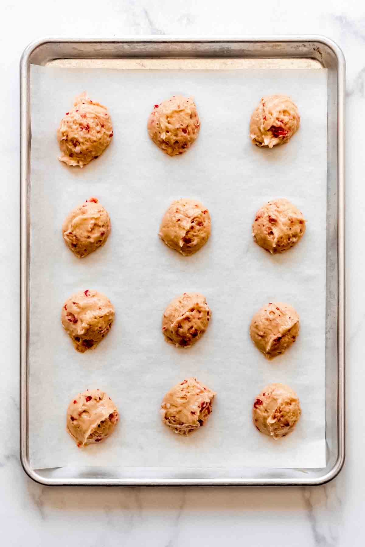 Strawberry whoopie pie batter scooped onto a parchment lined baking sheet.