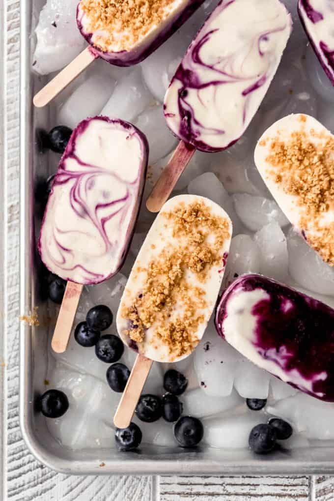 blueberry cheesecake popsicles with graham cracker crumbles on top on ice with blueberries