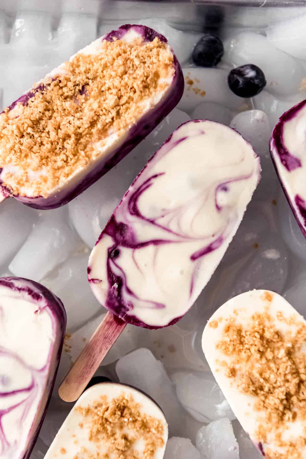 Close up of swirled creamy blueberry popsicles resting on ice. 