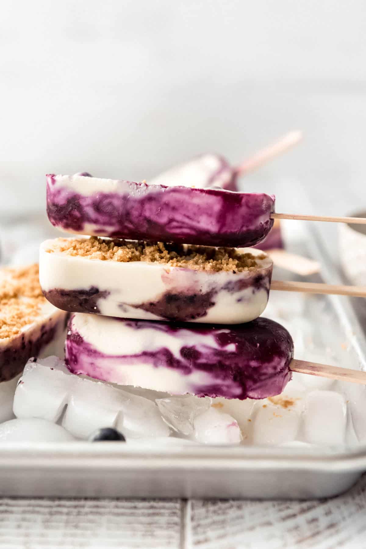 Three homemade blueberry cheesecake ice pops stacked on each other, resting on ice. 