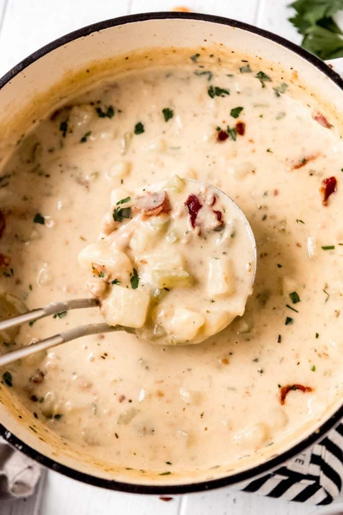 a dutch oven filled with clam chowder and a ladleful of clam chowder