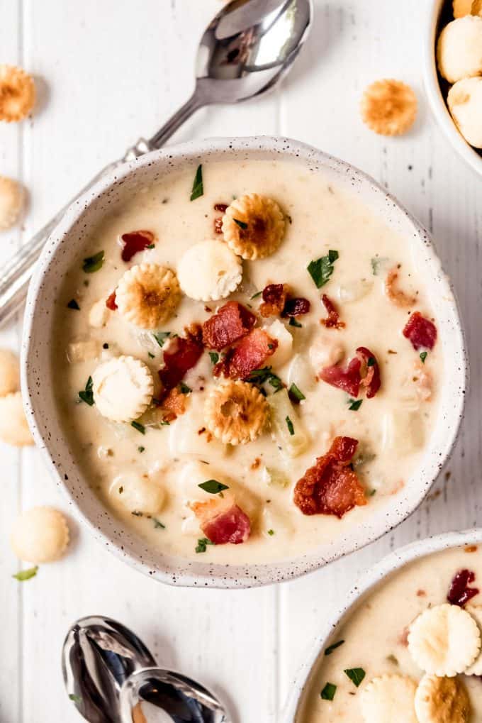 a bowl of clam chowder topped with oyster crackers, bacon, and parsley on top of a white table with a spoon