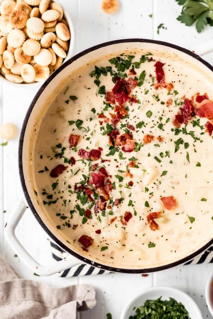 New England Clam Chowder in a dutch oven, sprinkled with crispy bacon and fresh parsley and a side of oyster crackers in a bowl