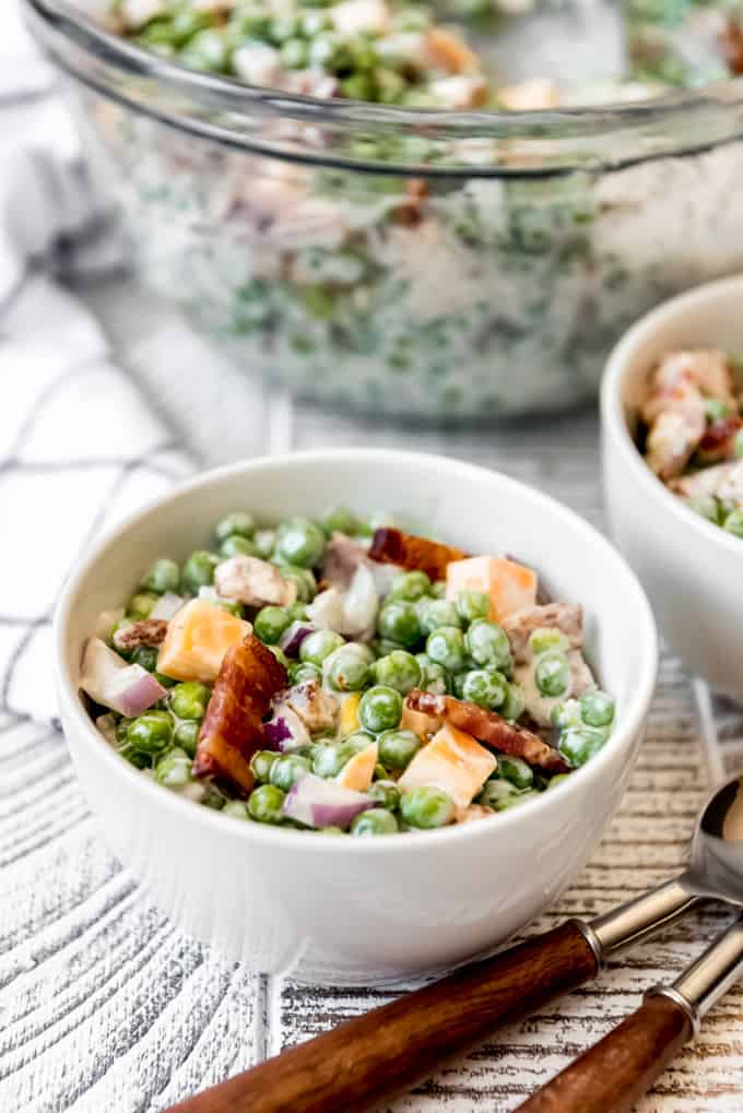 a small white bowl filled with a serving of pea salad with bacon and cheese