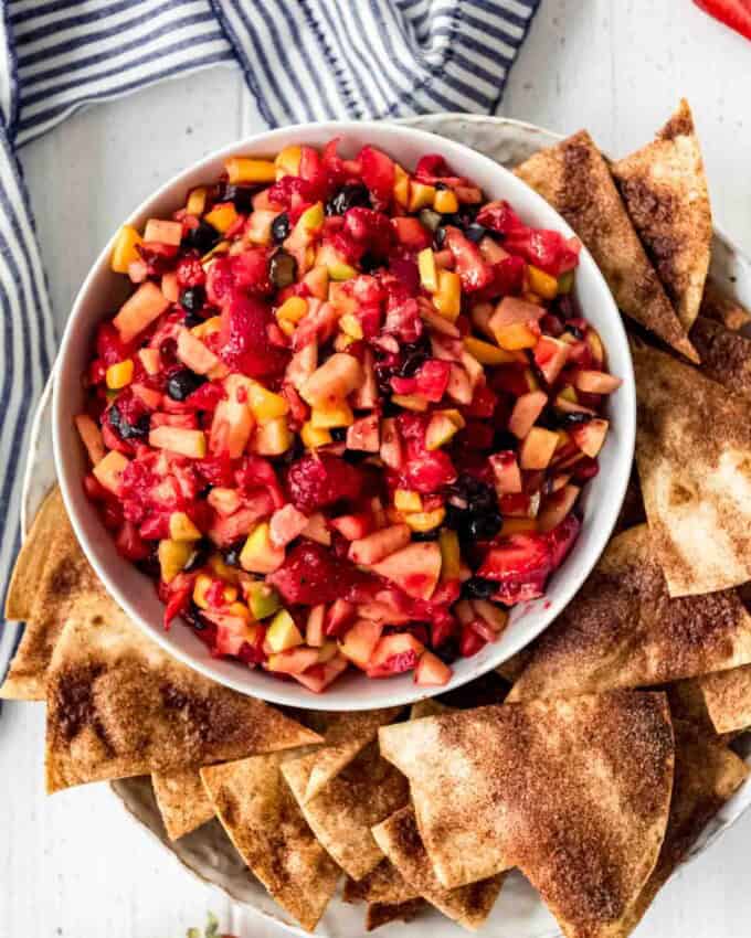 A bowl of fresh fruit salsa is displayed with crunchy cinnamon chips scattered around the bowl.