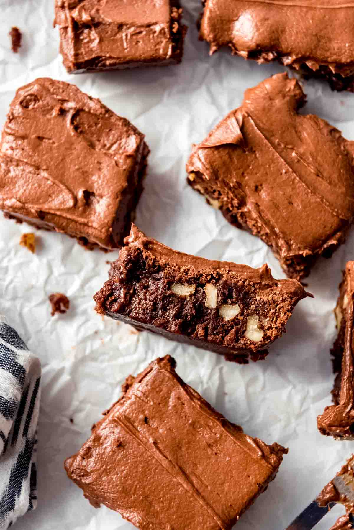 A brownie with walnuts and frosting on its side next to other frosted brownies.