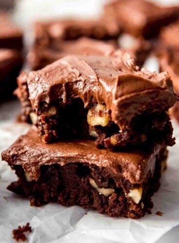 Two frosted brownies stacked with a bite taken out of the top brownie.