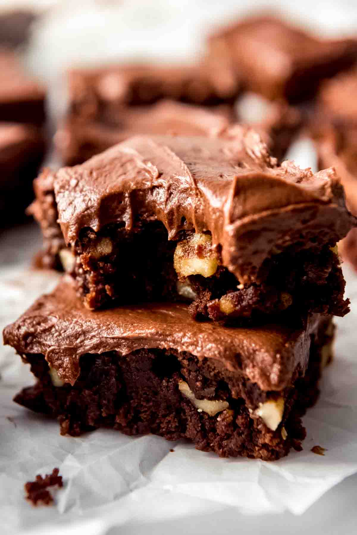 Two frosted brownies stacked with a bite taken out of the top brownie.