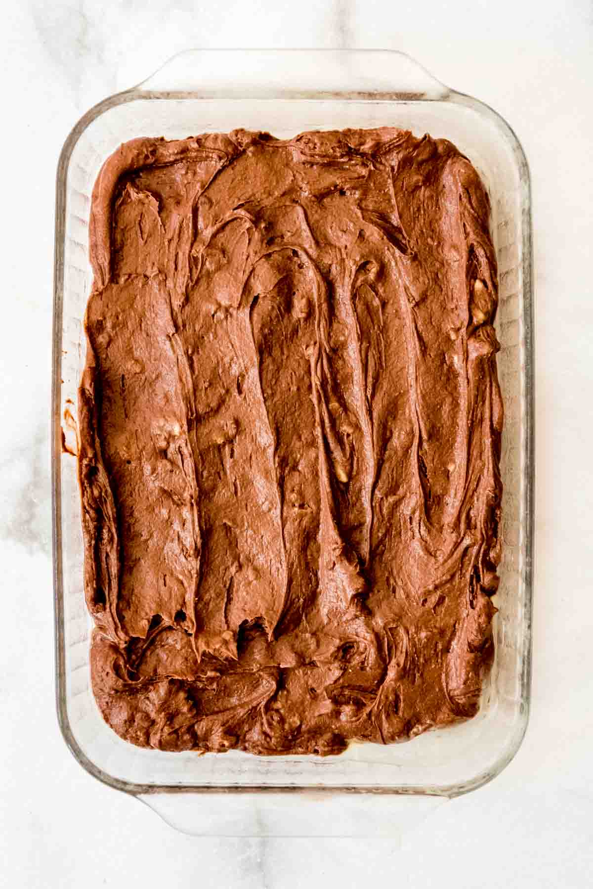 Mixed brownie batter has been poured and leveled in a glass 9 by 13 prepared pan. 