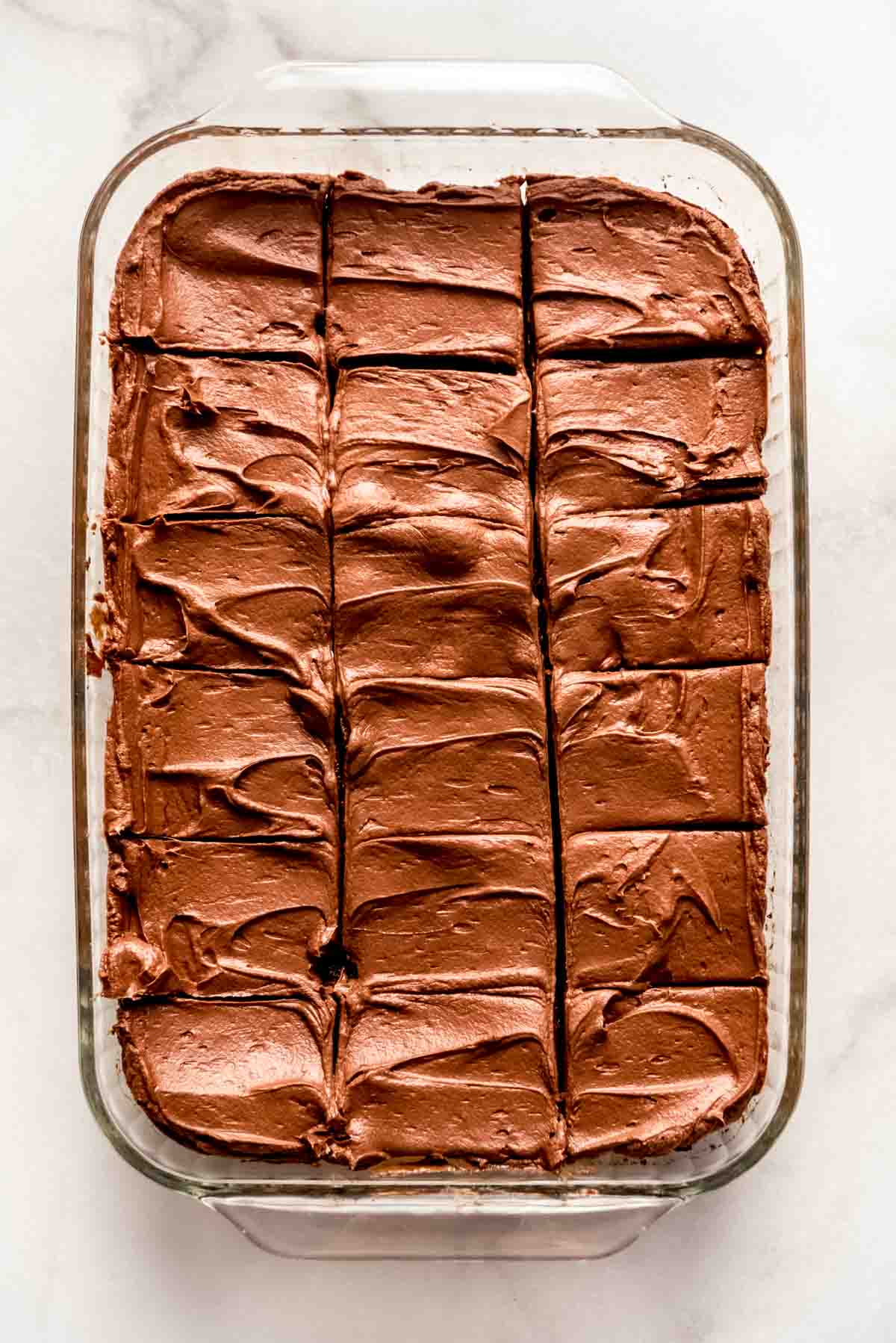 Cooked brownies have been removed from the oven and are resting on a white marbled surface, cooling before frosting is added. 