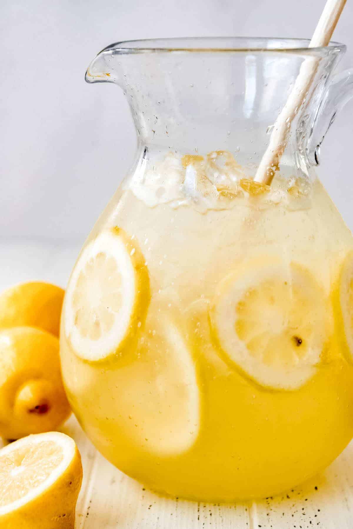 a close image of a glass pitcher filled with ice, sliced lemons, and lemonade