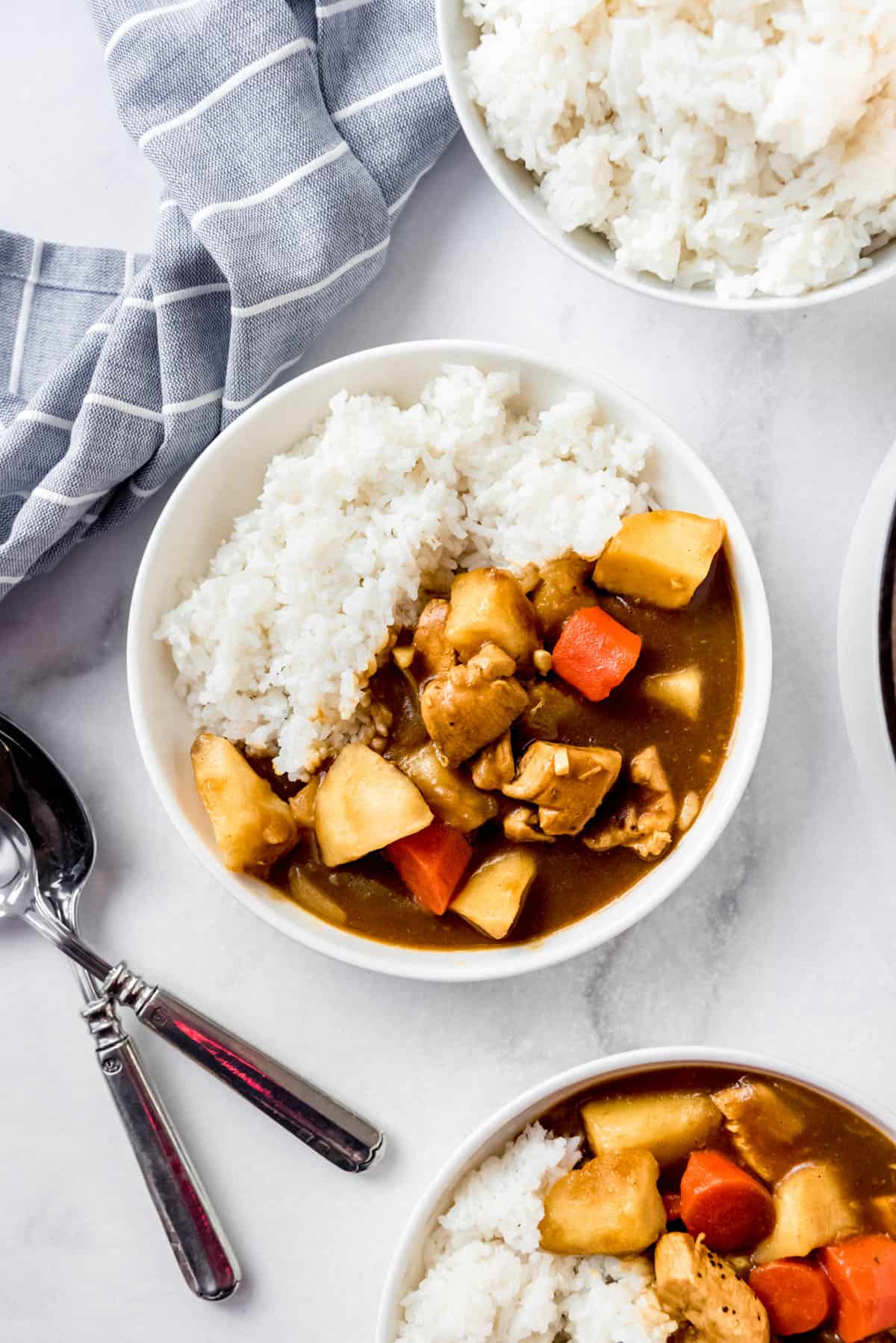 Overhead image of two bowls of curry and rice, with a bowl of plain rice visible in the top of the image. 