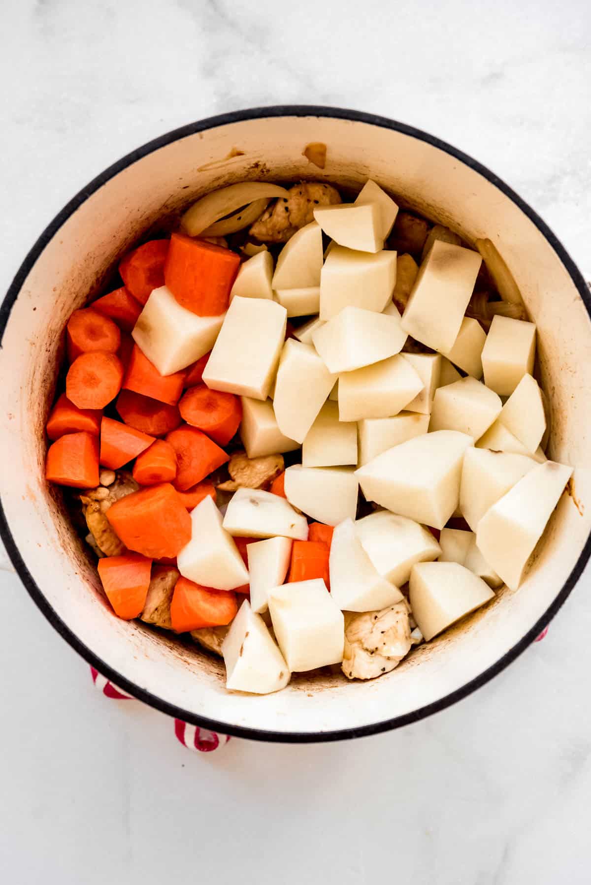 Diced carrots and cubed potatoes are added to the chicken and onion in the dutch oven. 