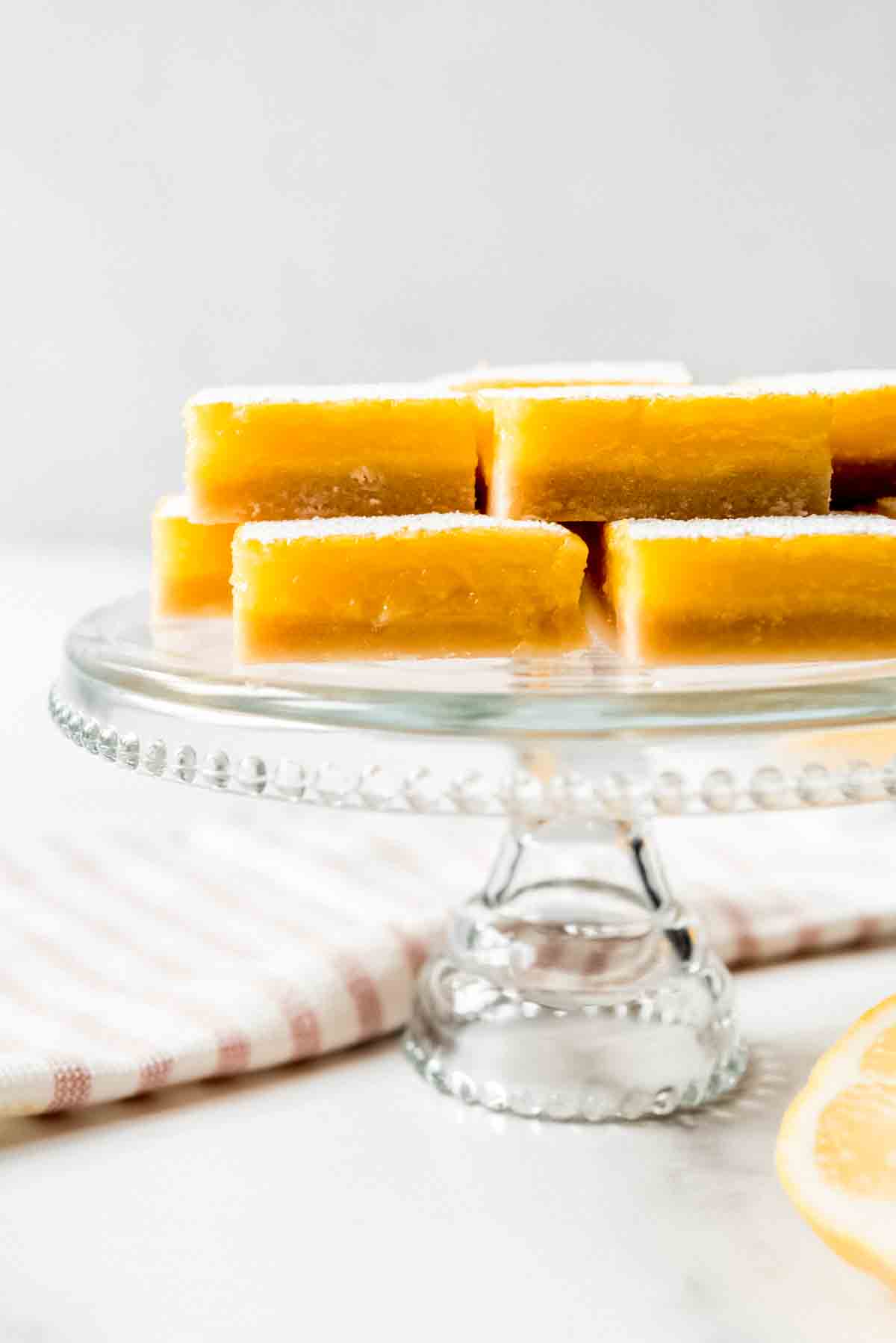 Lemon squares stacked on a glass cake stand.