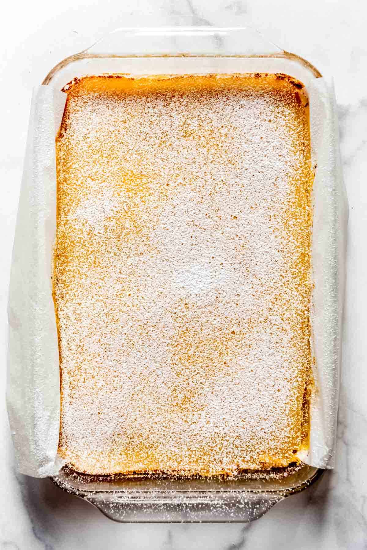 Cooked lemon bars in a nine by thirteen inch pan have been cooled and then dusted with powdered sugar. 