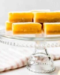 Lemon squares stacked on a glass cake stand.