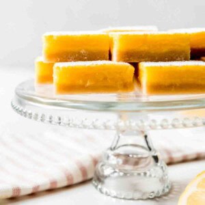 Lemon squares stacked on a glass cake stand.