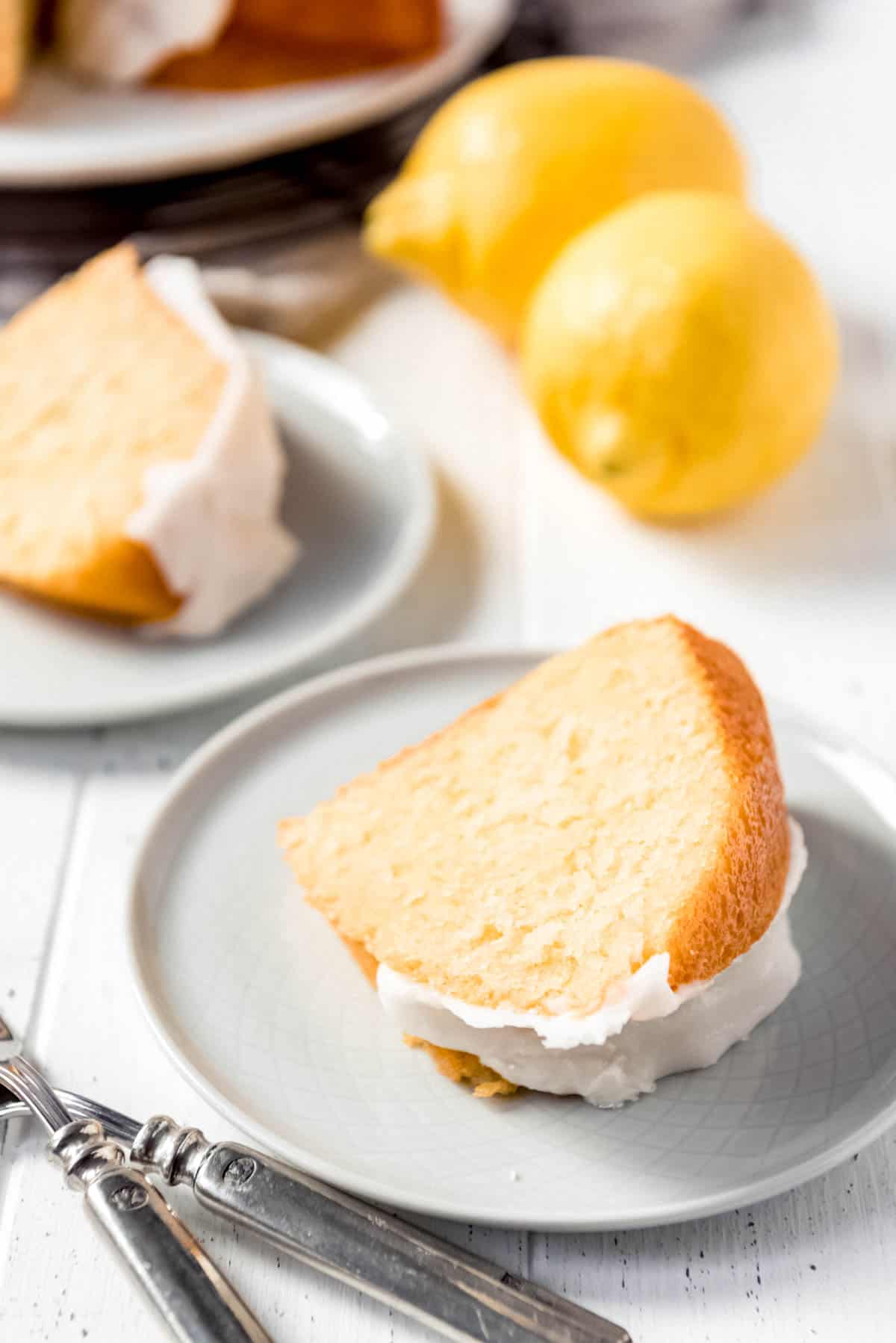 a slice of lemon bundt cake on a white plate  in front of lemons