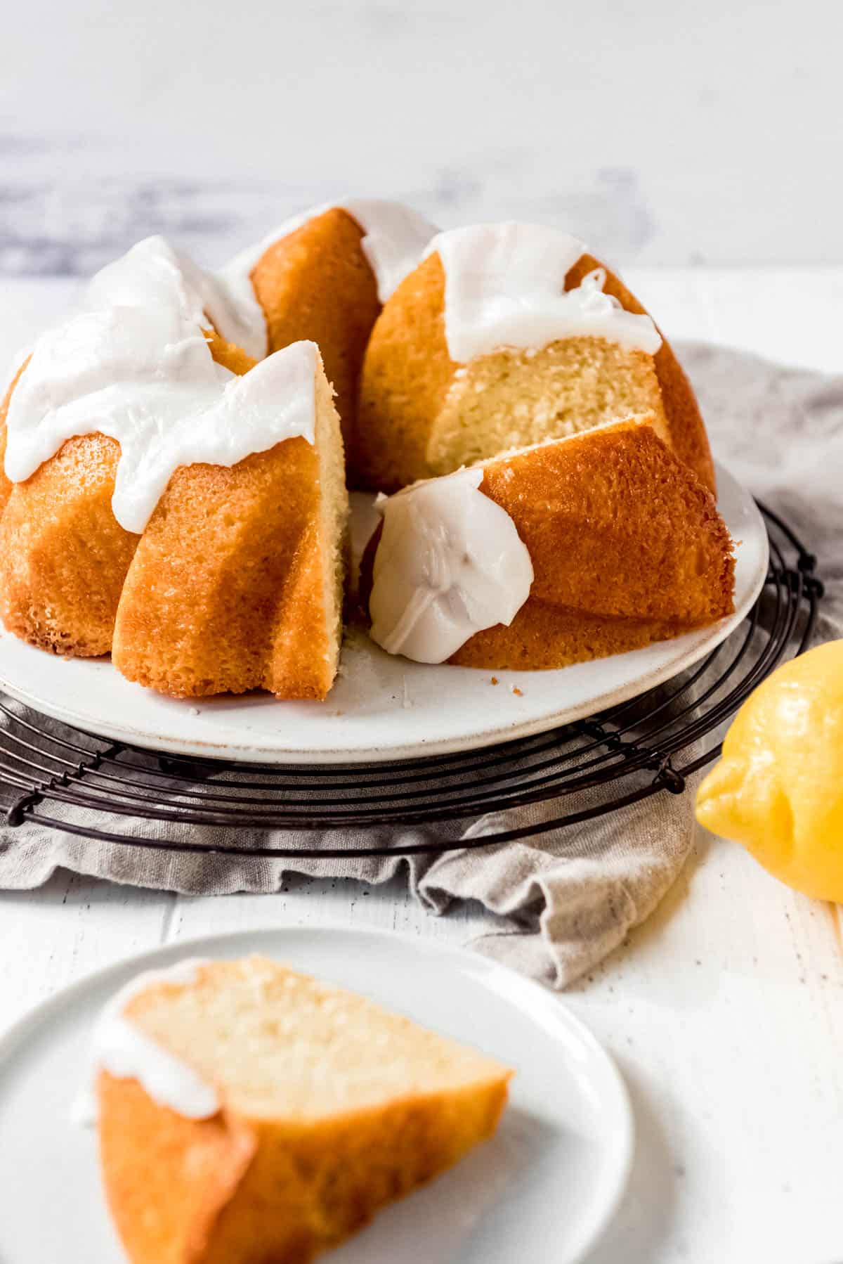 A lemon bundt cake is displayed on a plate, with a large slice turned on its side. 