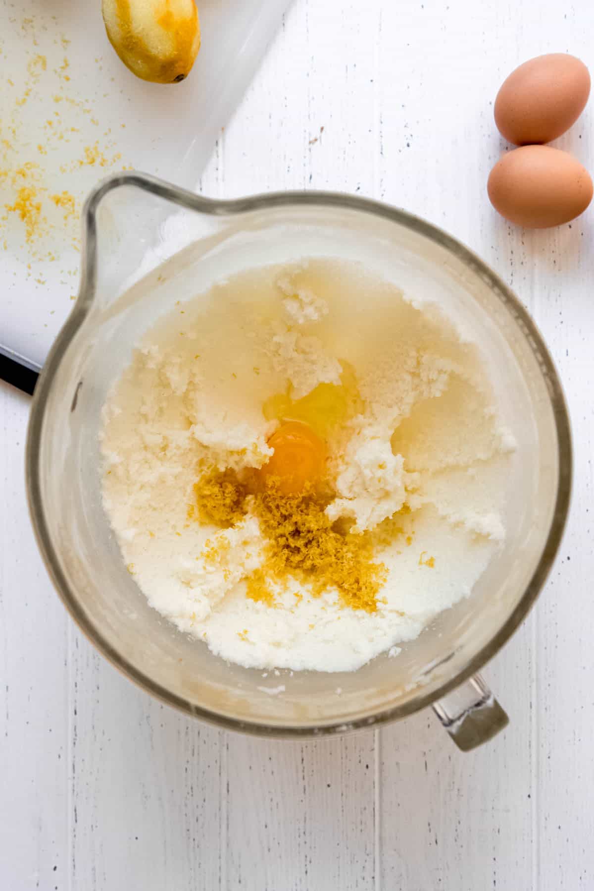 Adding eggs and lemon zest to a creamed butter and sugar mixture. 