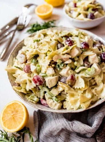 Side shot of Lemon Tarragon Pasta Salad, in stoneware bowl next to lemon and tarragon, with smaller bowl in background