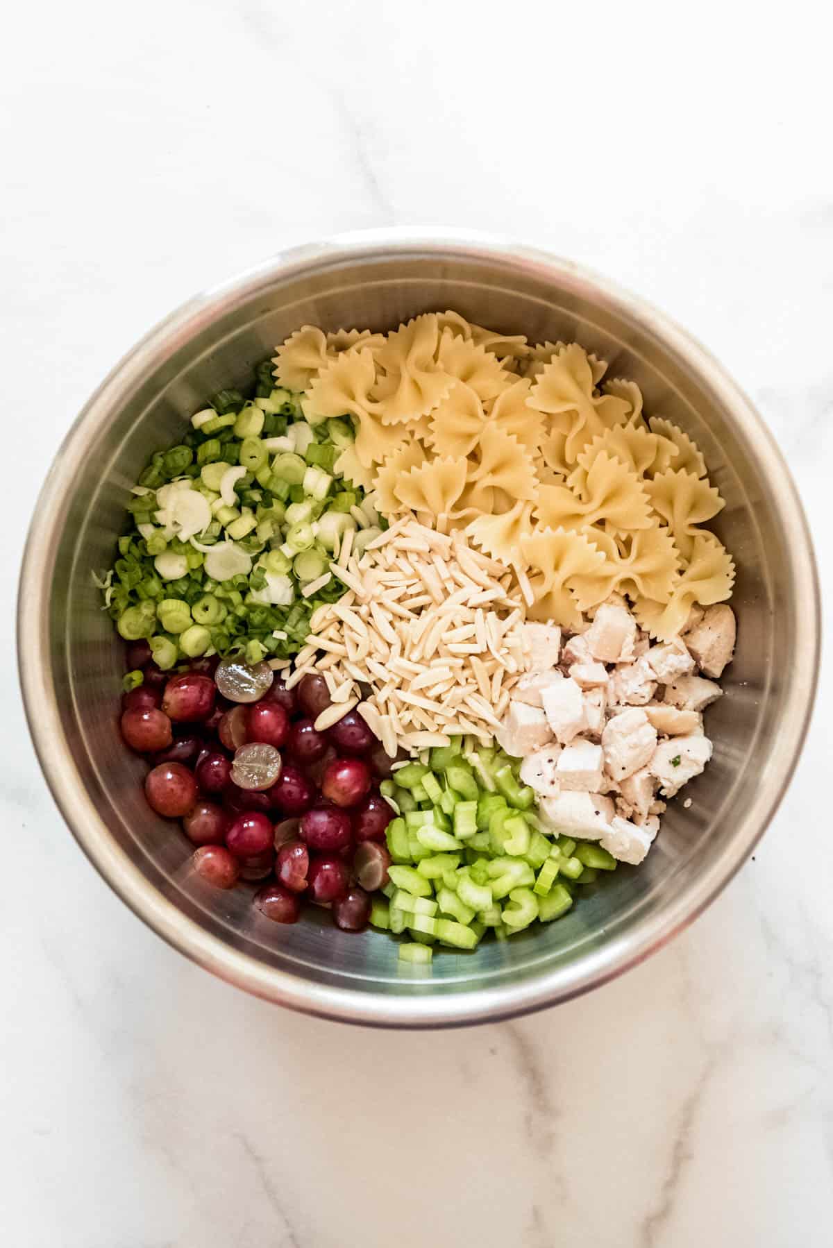 A large bowl filled with ingredients for making a chicken pasta salad with grapes.