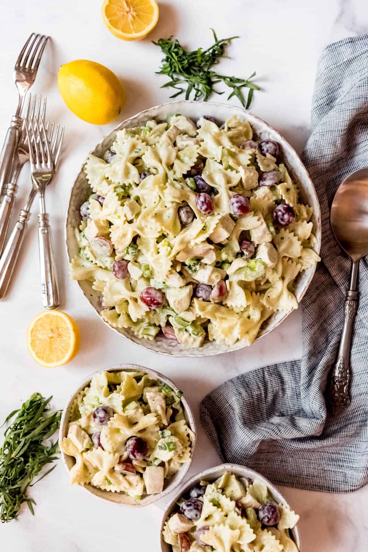 Overhead shot of Lemon Tarragon Pasta Salad, in stoneware bowl next to two smaller bowls of pasta salads, forks and a spoon