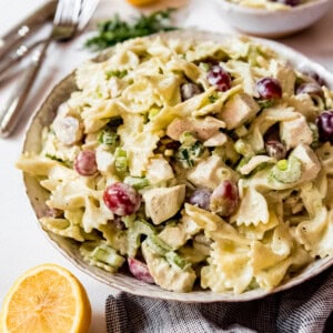 Side shot of Lemon Tarragon Pasta Salad, in stoneware bowl next to lemon and tarragon, with smaller bowl in background