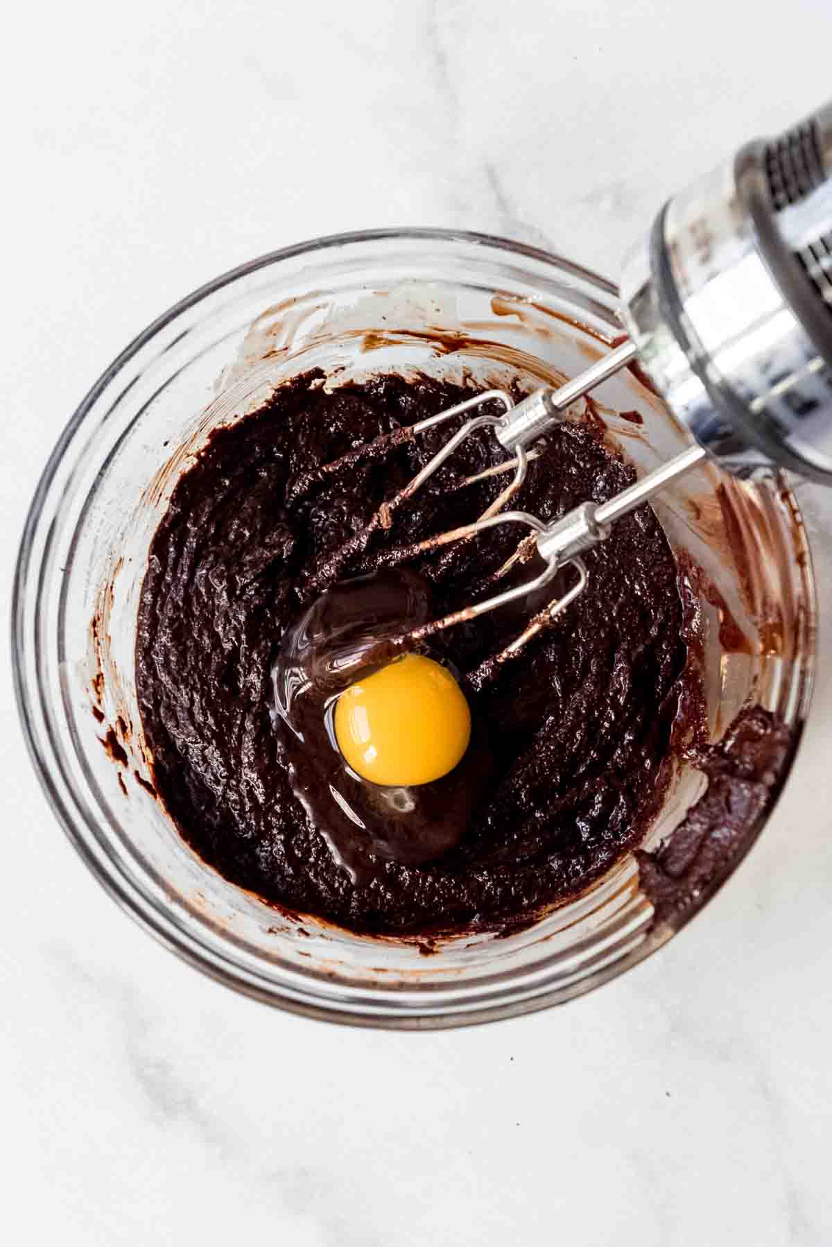 An overhead image of an egg being added to brownie batter.