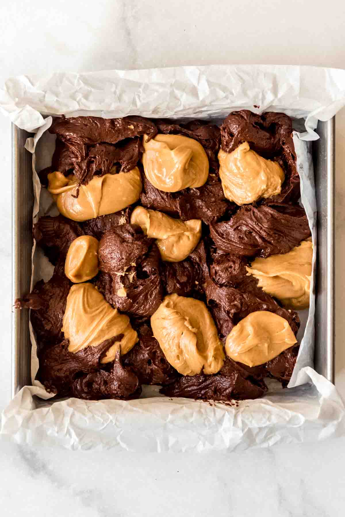 Alternately adding drops of brownie batter and peanut butter mixture to a square pan.