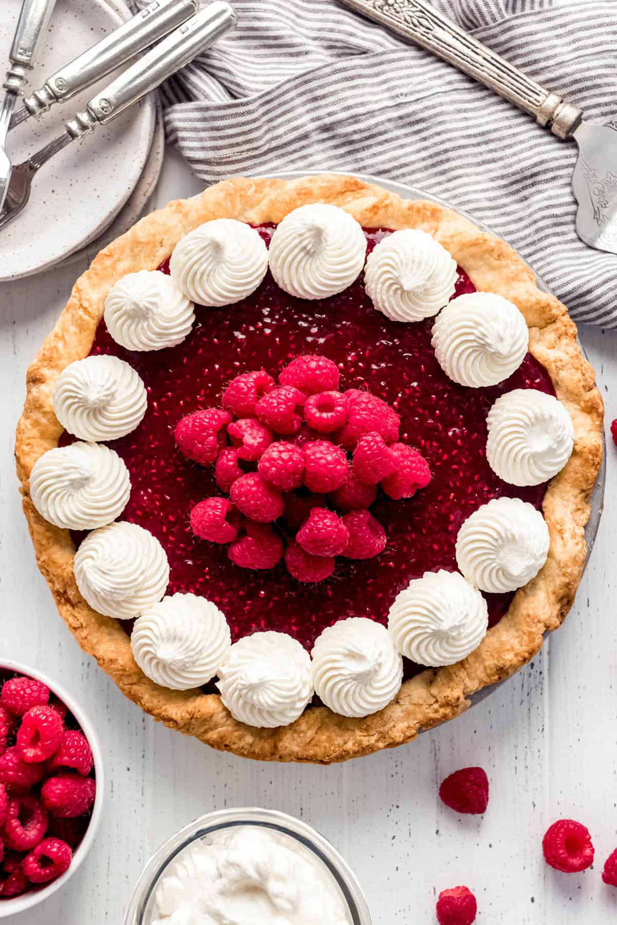 a raspberry cream pie topped with swirls of whipped cream and fresh raspberries
