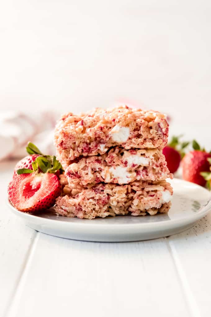A stack of 3 strawberry rice krispies treats with a fresh strawberry on a white plate