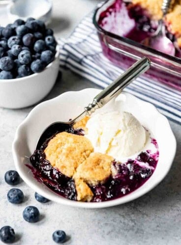 An image of a white bowl filled with blueberry cobbler and ice cream.