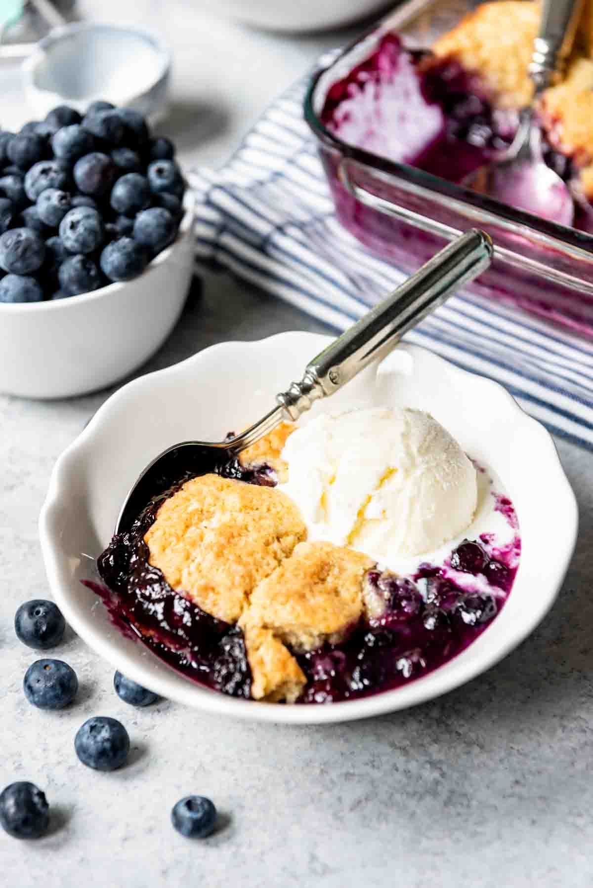 An image of a white bowl filled with blueberry cobbler and ice cream.