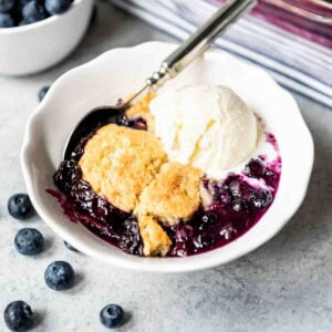 An image of a white bowl filled with blueberry cobbler and ice cream.