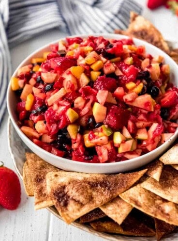 A bowl of fruit salsa with cinnamon chips on the side.