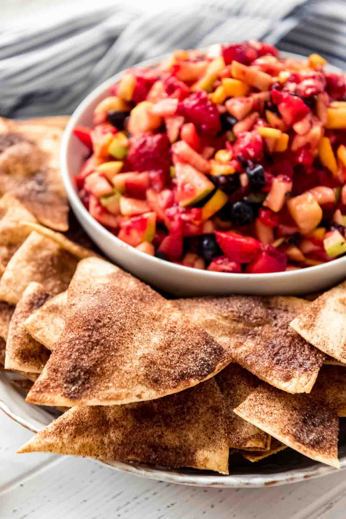 A bowl of fresh fruit salsa is displayed with crunchy cinnamon chips scattered around the bowl. 