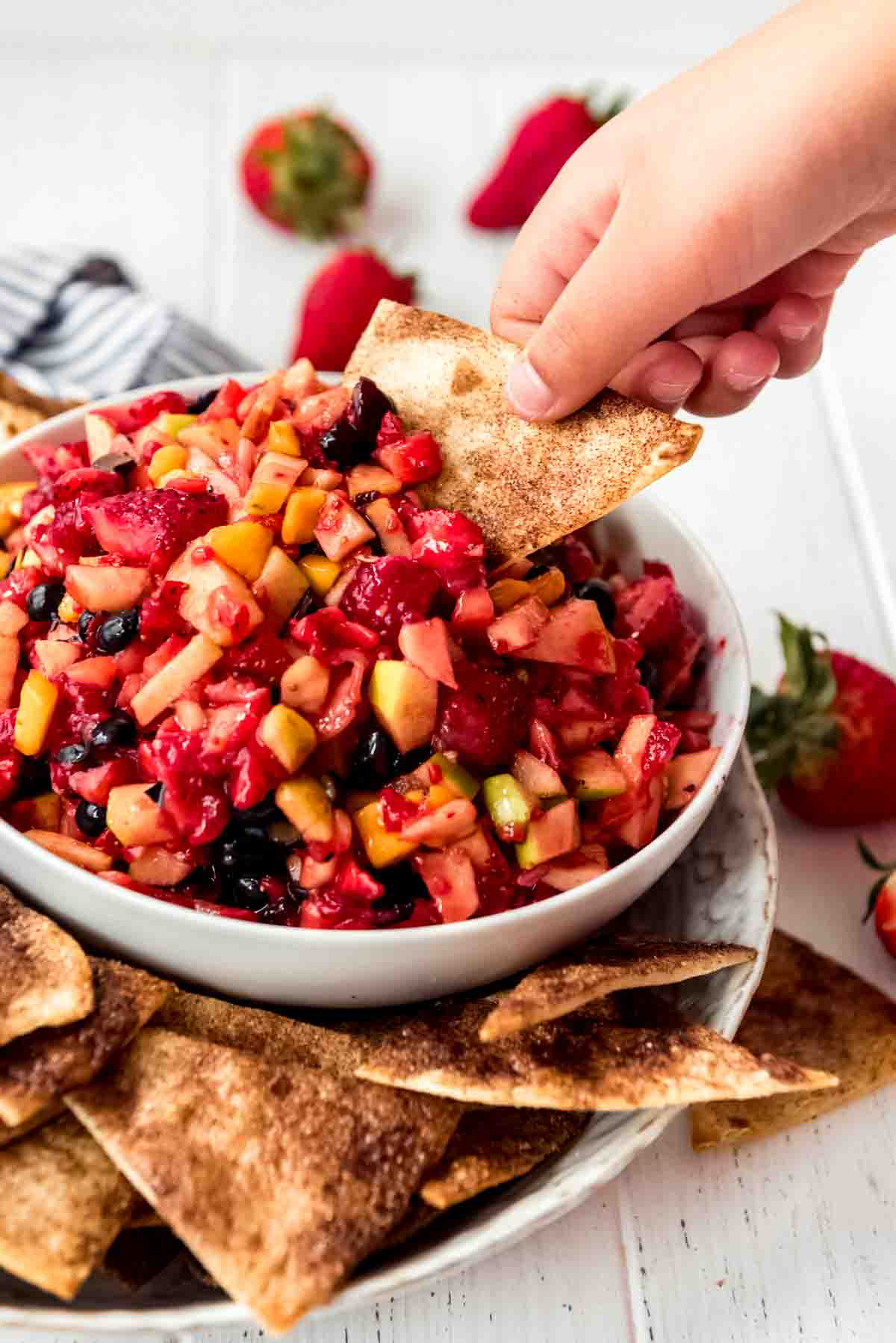 A hand holding a cinnamon chip to scoop fruit salsa out of a bowl.