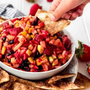 A bowl of fresh fruit salsa is displayed with crunchy cinnamon chips scattered around the bowl.